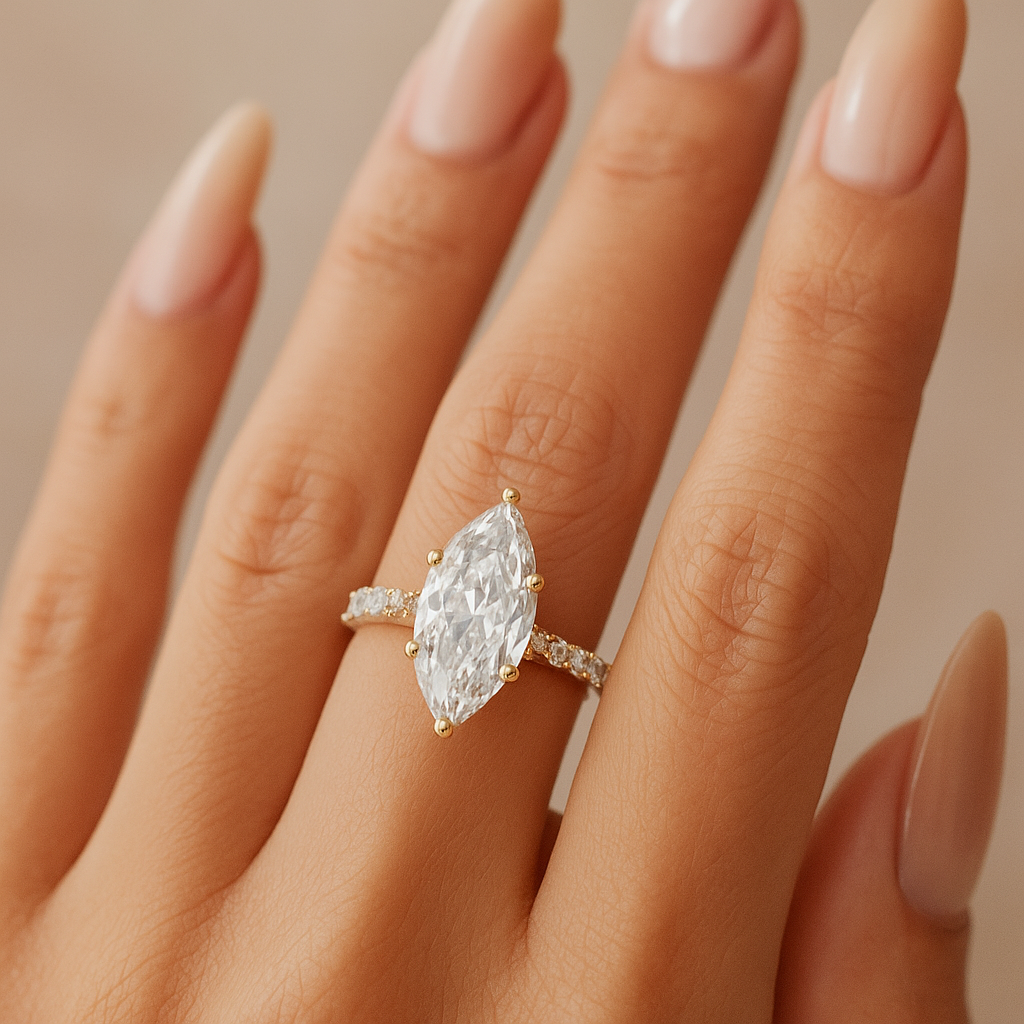 Close-up of a hand wearing a 14K yellow gold marquise lab diamond engagement ring with hidden halo and pavé band photographed on warm neutral background