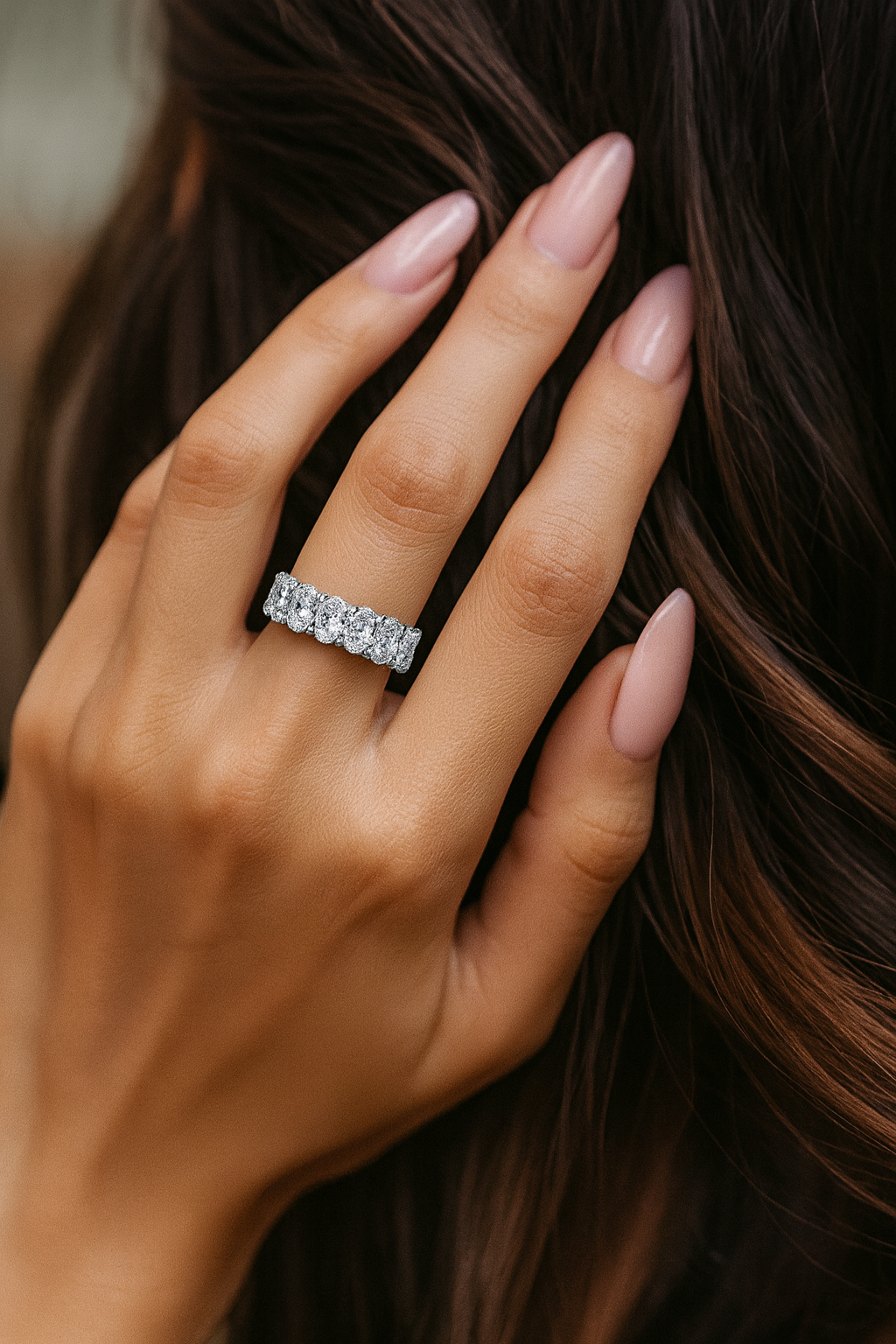 Woman’s hand with long blush-pink almond nails wearing a 4.00ct oval lab-grown diamond eternity band in 14K white gold, shown in a lifestyle close-up