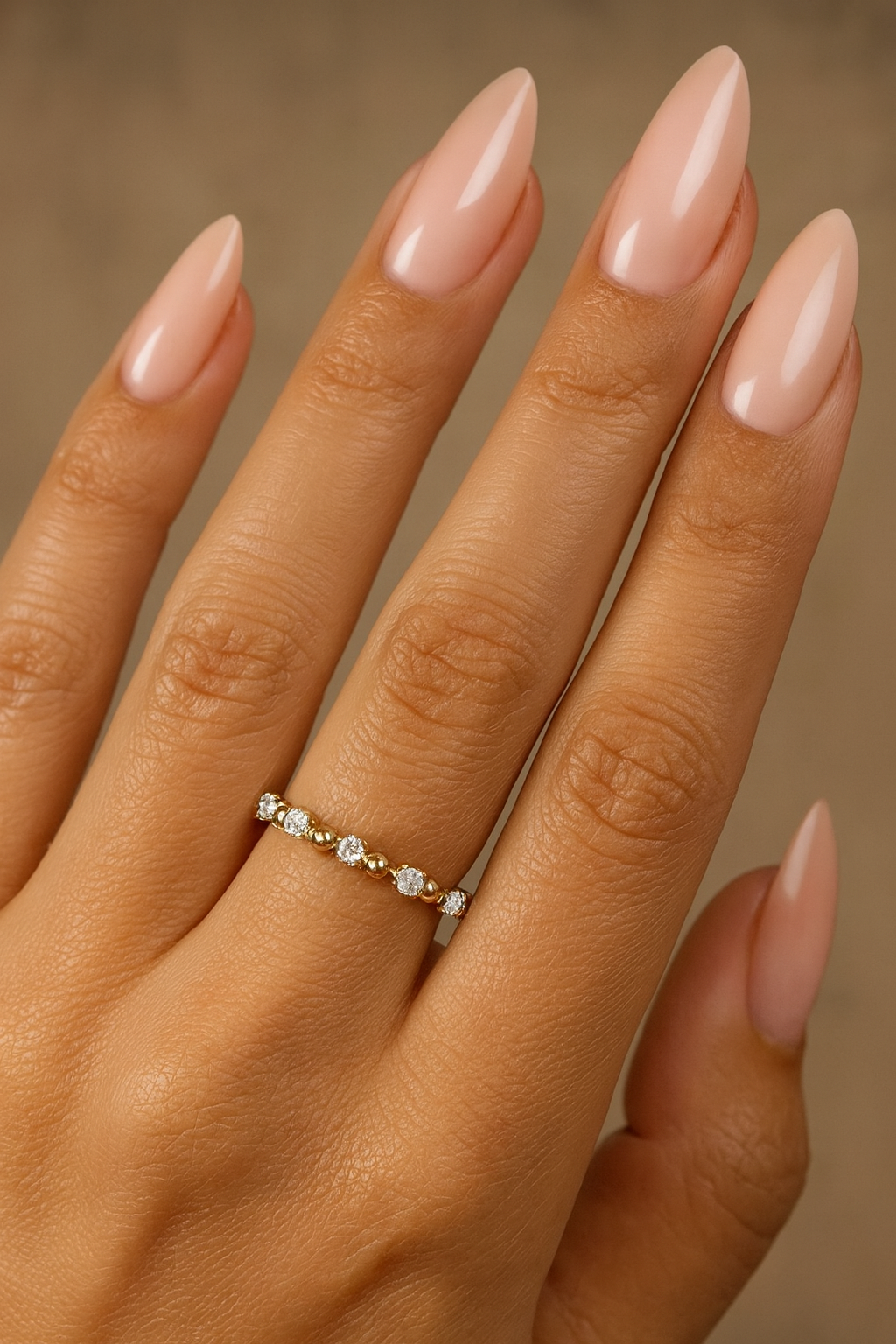 Beaded diamond wedding band in 14K yellow gold on model’s hand with almond-shaped nude nails