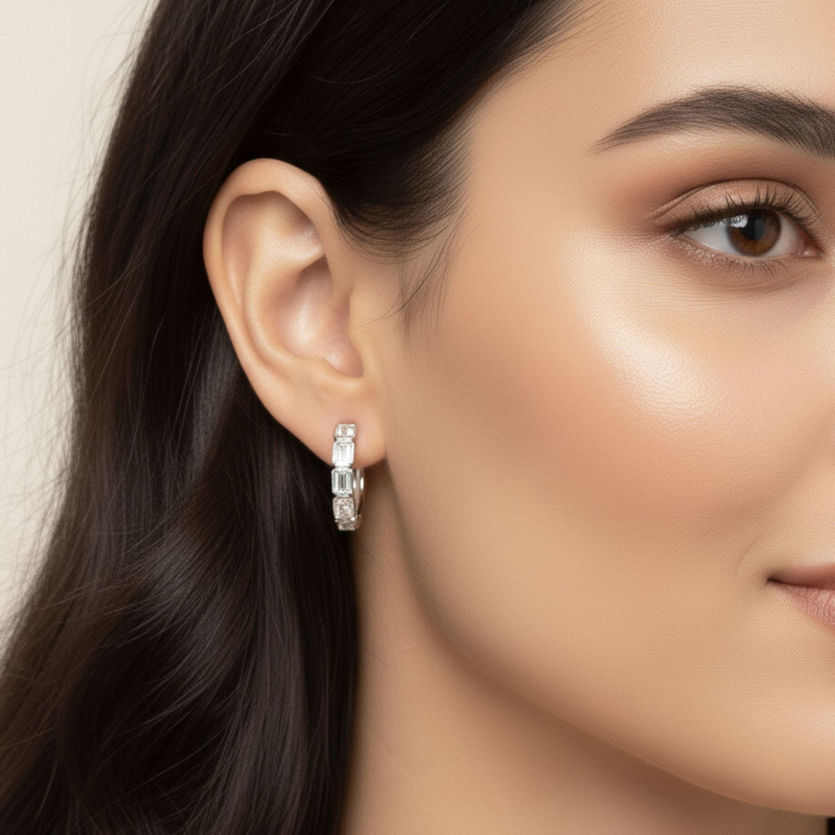 Close-up of a white gold emerald-cut diamond bezel hoop earring worn on the ear