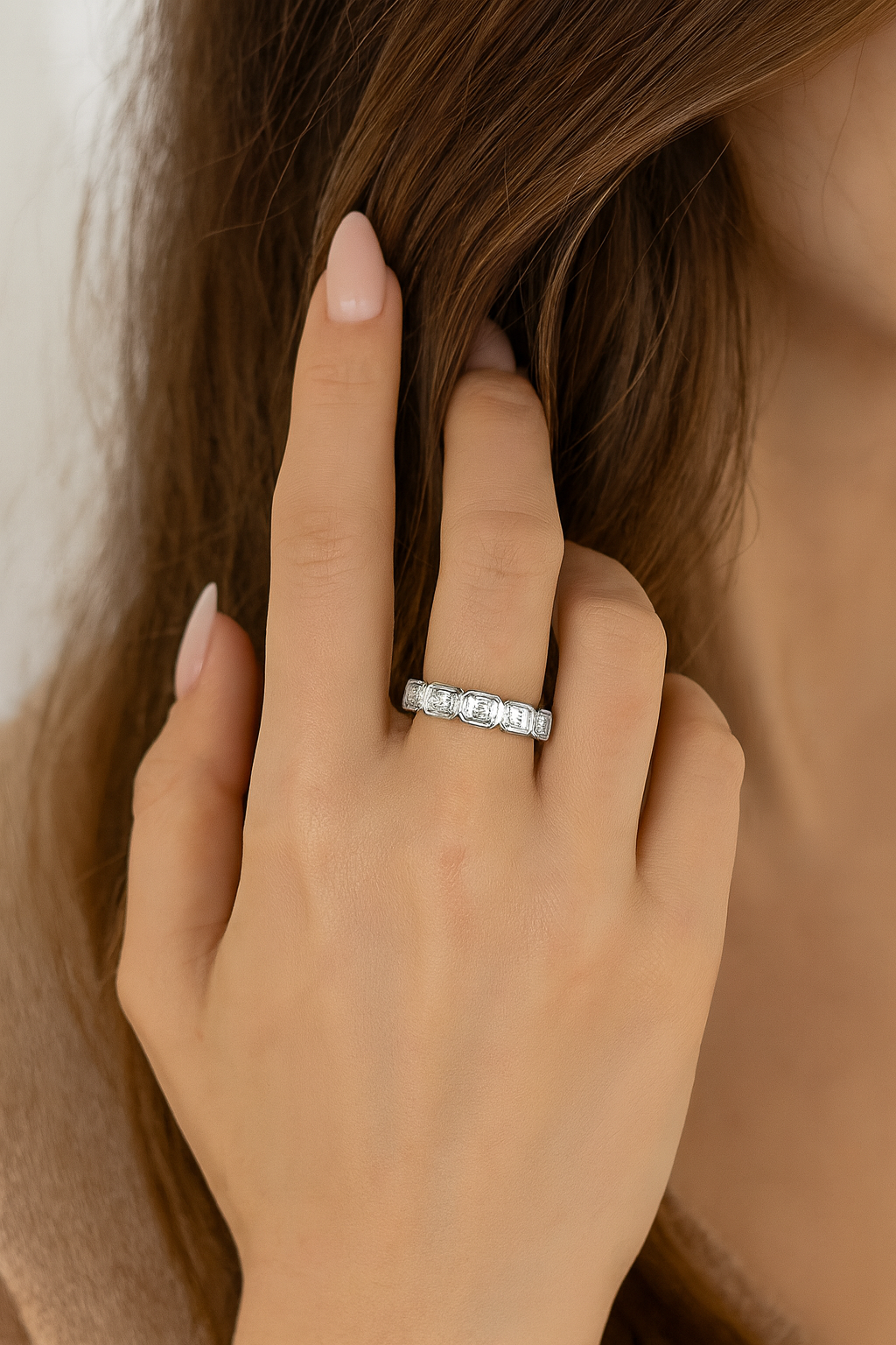 Woman wearing an elongated emerald-cut lab diamond bezel eternity band in 14K white gold, shown on hand with soft almond-shaped nails for size and sparkle reference.